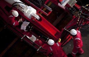 Over head photograph of 3 Houlder engineers operating and testing off shore wind energy equipment to be attached to a vessel. All three workers are wearing Houlder uniform personal protective equipment (PPE). The image was shot from a scissor lift in one of Houlder's warehouses in Tynemouth.