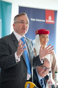 Professional commercial shot showing a speaker standing and talking with a woman smiling the background, out of focus. Shot by professional northeast commercial photographer Cal Carey.