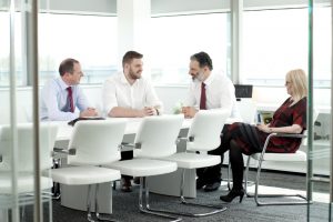 A professional shot of four workers sat conversing around a table. Shot by professional northeast commercial photographer Cal Carey.
