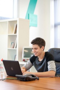 Portrait professional advertising photography shot showing a VIA Creative worker sat at his desk, working on the computer, smiling. Shot by professional northeast advertising photographer Cal Carey.
