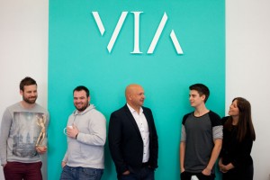 Professional advertising photography shot showing five VIA Creative employees standing in below the VIA logo on a turquoise background. Shot by professional northeast advertising photographer Cal Carey.