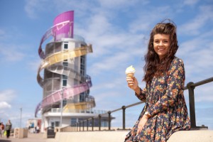 Professional advertising shot showing a girl, with a lemon top sat down on one of the sea defences with the Redcar Beacon in the background. Shot by professional advertising photographer Cal Carey.