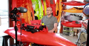 Behind the scenes shot showing the subject male with a canoe in front of him whilst many are around.
