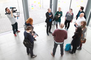 Behind the scenes shot showing Cal Carey Photographer using a DSLR on a shoulder rig to film a group of people at MIMA.