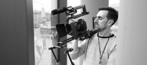 Black and White behind the scenes photography shot showing Cal Carey Photographer using a shoulder rig with a DSLR on it and rode mic.