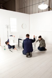 Behind the scenes photography shot showing three people on set sorting a table and chairs ready to be shot.