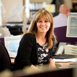 Professional corporate people shot of a woman sat down but just angled away from her desk. She's looking just beyond camera, smiling. Shot by professional northeast corporate photographer Cal Carey.