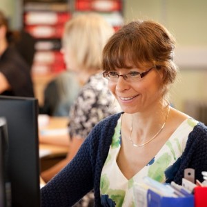 Professional corporate people shot of a woman sat at a desk looking at her computer, smiling. Shot by professional northeast corporate photographer Cal Carey.