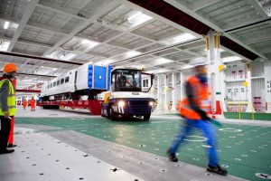 Professional industrial and transport shot of a Hitachi train being loaded out of the ship by vehicle. Worker in high-visability clothing in the foreground as he's moving. Shot by professional north-east photographer Cal Carey.