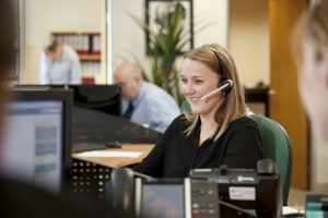 Professional commercial photography shot showing a woman at her desk talking on her headset to a client. Shot by professional northeast commercial photographer Cal Carey.