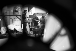 Behind the scenes, black and white, shot looking through a wheel rim to show the rear of the car along with Cal Carey Photographer and engineers.