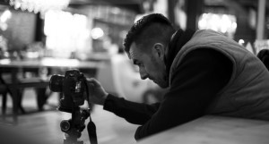 Black and white behind the scenes shot showing professional advertising photographer Cal Carey crouching and looking at the screen on his DSLR camera.