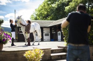 Behind the scenes photography shot showing an out of focus Cal Carey shooting the subject which is an in focus view of two girls with a horse.