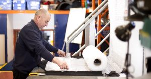 Professional industrial photography shot showing a man at the packing station wrapping a product for a customer ready to be shipped. Shot by professional northeast industrial photographer Cal Carey.