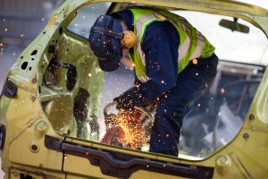 Professional industrial photography shot showing an engineer in high-vis and ear defenders using a power tool to cut a car whilst sparks are flying. Shot by professional northeast industrial photographer Cal Carey.
