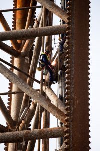 Professional industrial shot showing a man welding on the structure of an oil rig. He is also working off ropes. Shot by professional northeast industrial photographer Cal Carey.