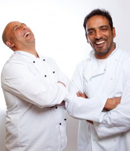 Professional commercial shot showing a mid-shot of two chefs, one of them with their head back laughing and the other smiling straight into camera. Shot by professional northeast commercial photographer Cal Carey.