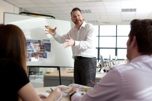 This is a professional photograph of the Velvet Communications brand manager enthusiastically presenting a project, with a whiteboard in the background and his two co-workers giving feedback and reacting to his project. Shot by professional northeast commercial photographer Cal Carey.