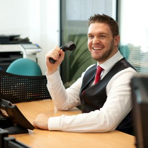 Professional commercial shot showing a man at his desk with a phone in hand, smiling. Shot by professional northeast commercial photographer Cal Carey.